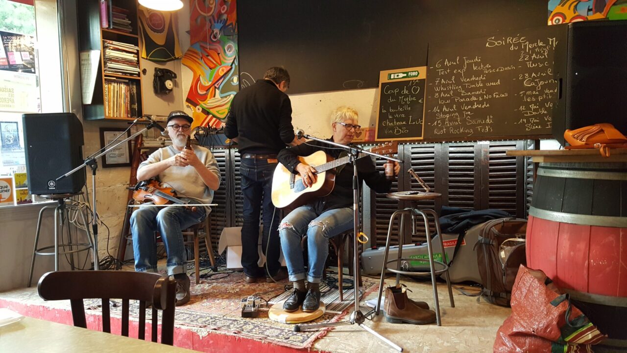 Dana et Claude assis sur scène avec violon et guitare dans un bar du Poitou