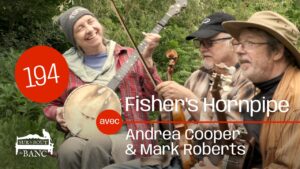 A woman and man playing banjos sit on a bench with a fiddler, outdoors with trees in background.
