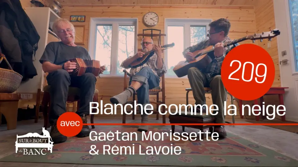 Trois hommes jouent de la musique traditionnelle dans une entrée de maison, sur concertina, mandoline et guitare.