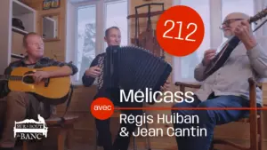 Trois hommes jouent guitare, accordéon et mandola dans une entrée en hiver.