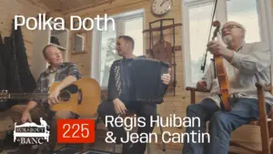 Trois hommes jouent de la musique trad dans une entrée de maison à la guitare, à l'accordéon et au violon