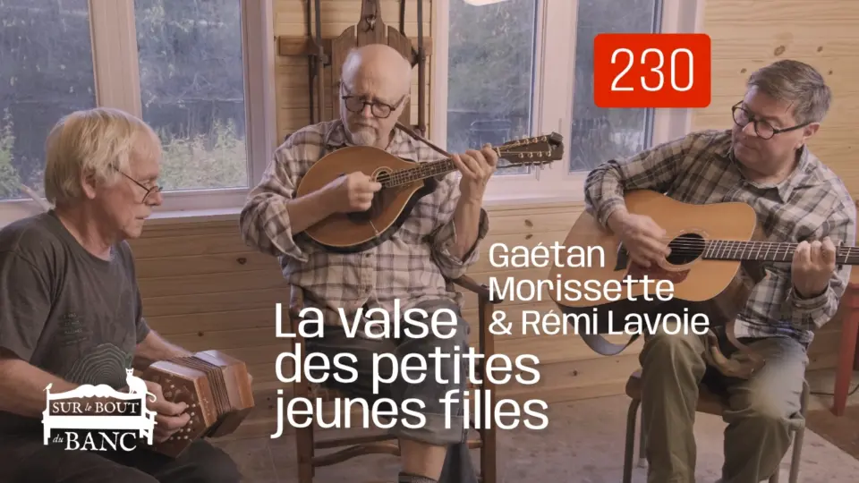 Trois hommes jouent concertina, mandola et guitare dans une entrée de maison.