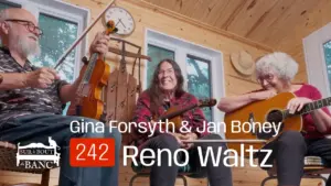 Deux femmes et un homme jouent violons et guitare dans une entrée de maison en chantant une chanson cadienne.